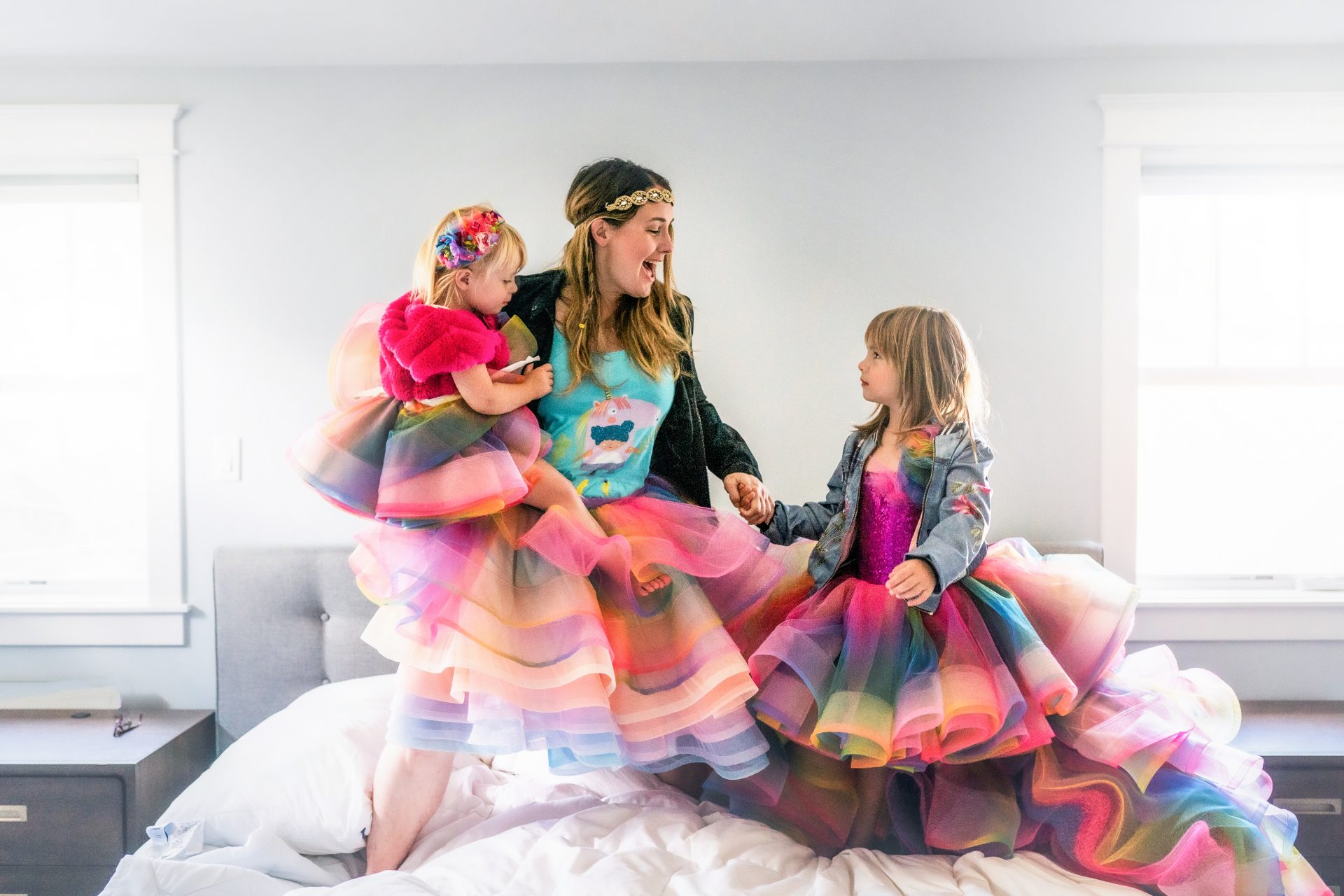 Mom and two daughters in rainbow dresses jumping on bed